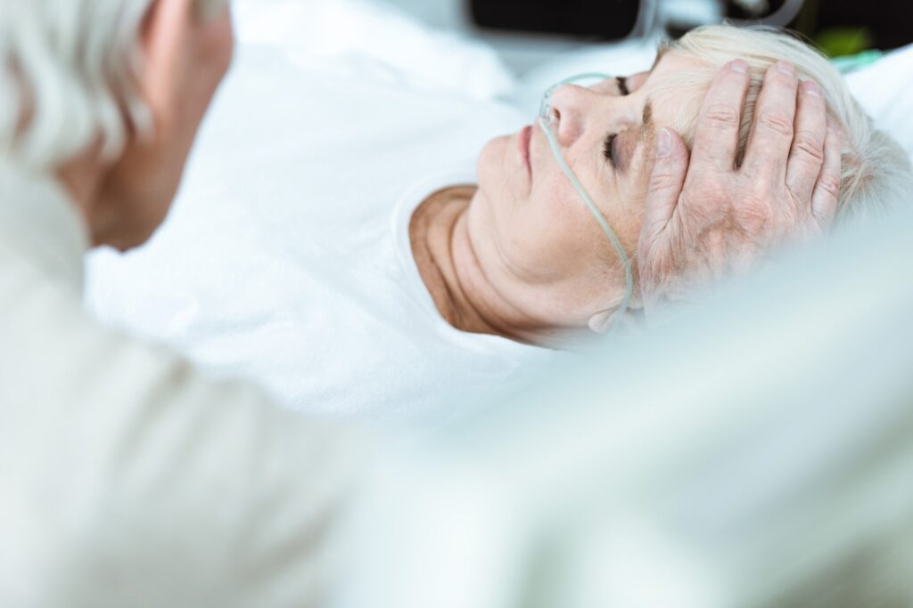 cropped view of senior man stroking wife in coma in clinic