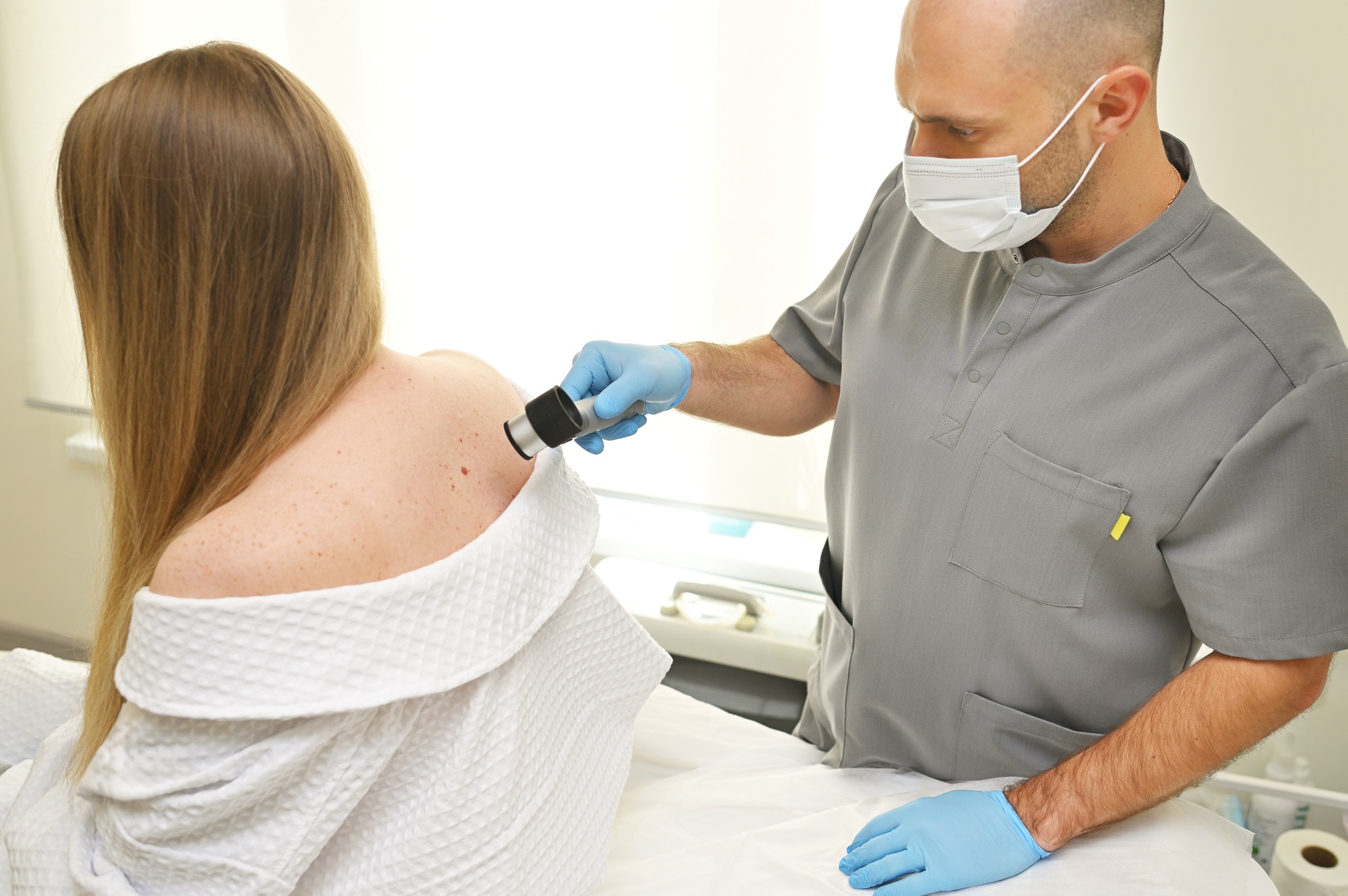 dermatologist examines neoplasms on the patient's skin using a special dermatoscope device