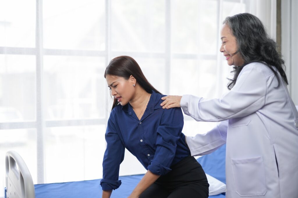 Doctor provides assistance to a woman experiencing back pain in a medical office.