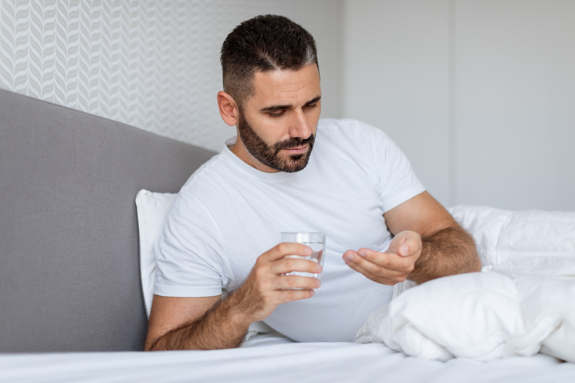 Guy Taking Pill Treating Severe Morning Headache Lying In Bed