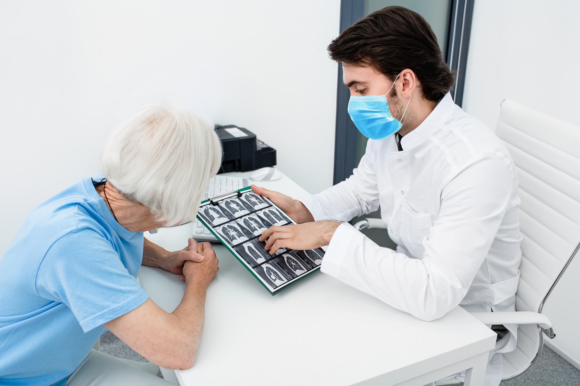 Pulmonologist wearing a surgery mask showing a senior patient a CT scan of her lungs. Pneumonia,
